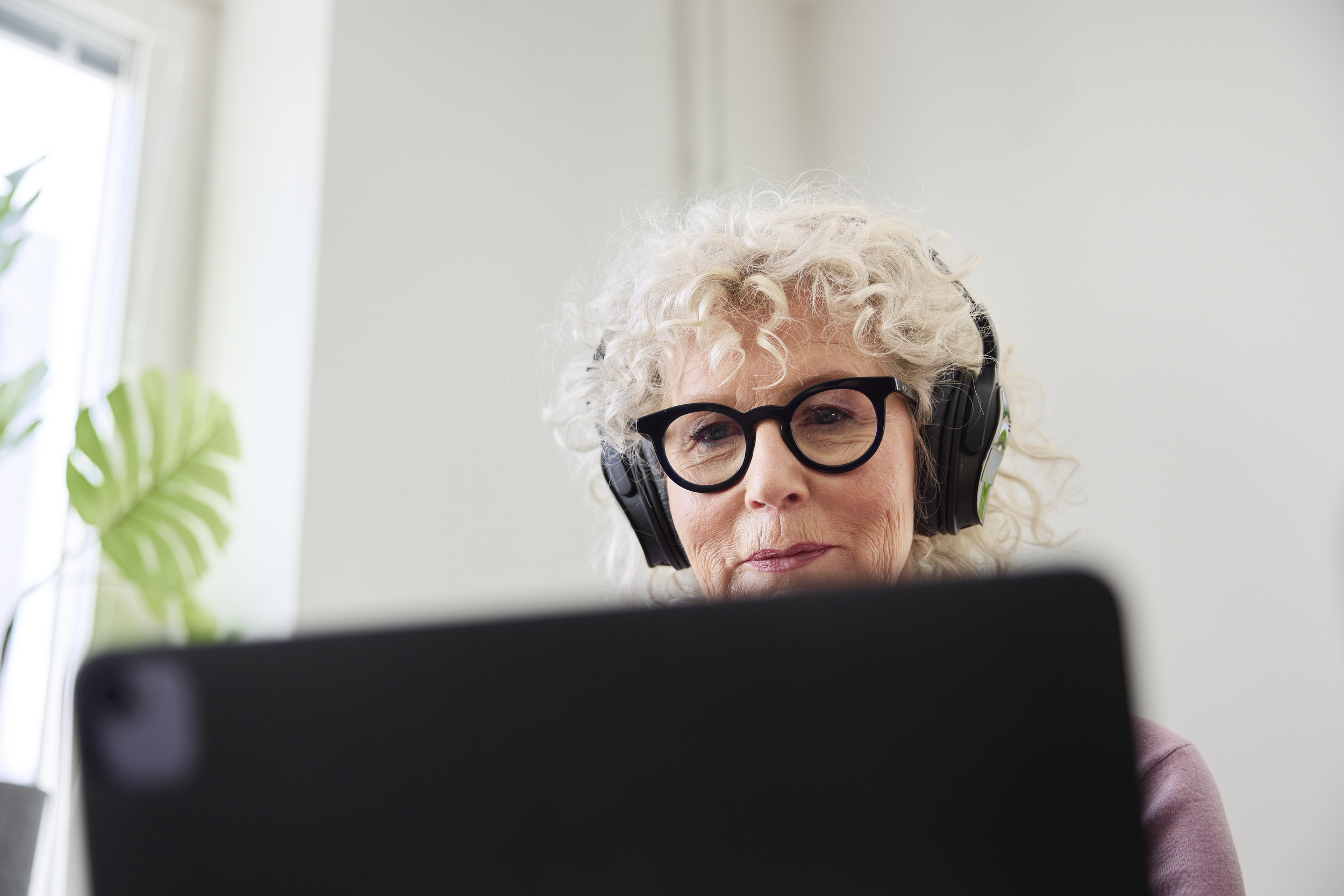 Äldre dam sitter med hörlurar och en laptop