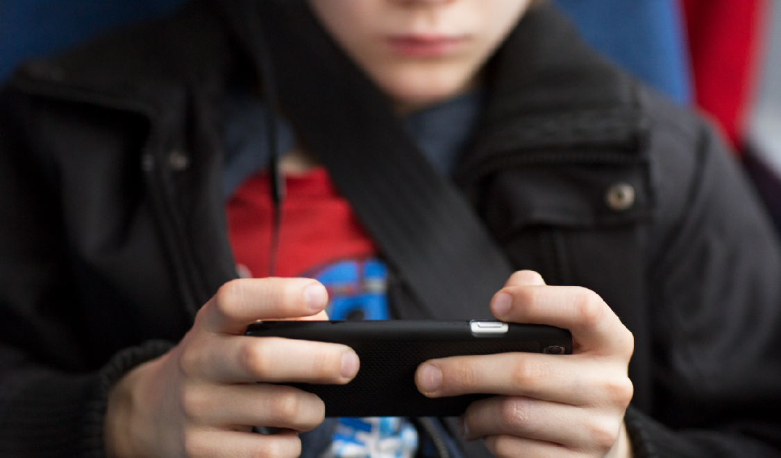 Ett barn sitter fastspänt med säkerhetsbälte och håller en smartphone med båda händerna