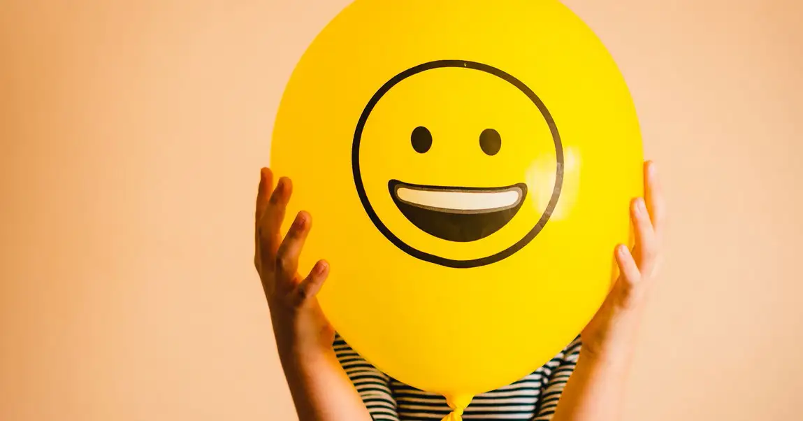 Person håller upp en gul ballong med ett stort smiley‑ansikte tryckt på