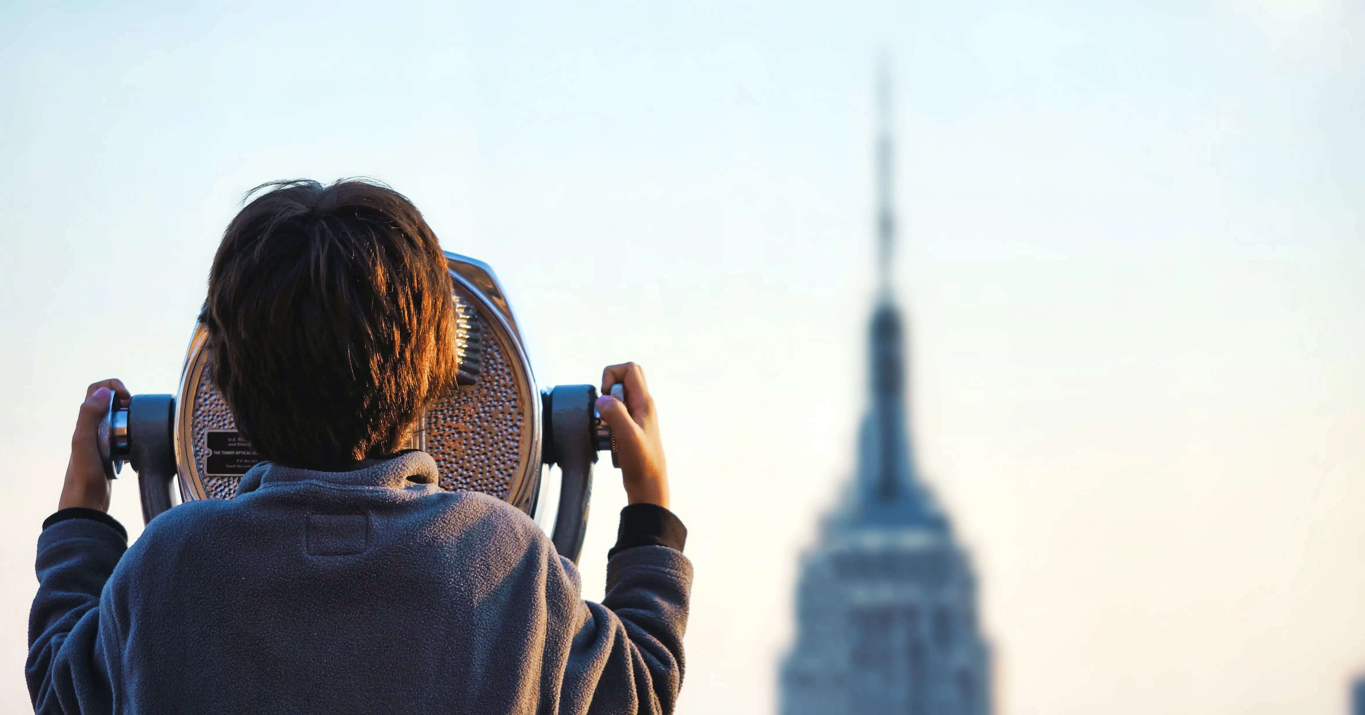 Person som tittar genom en utsiktskikare mot en avlägsen byggnad.