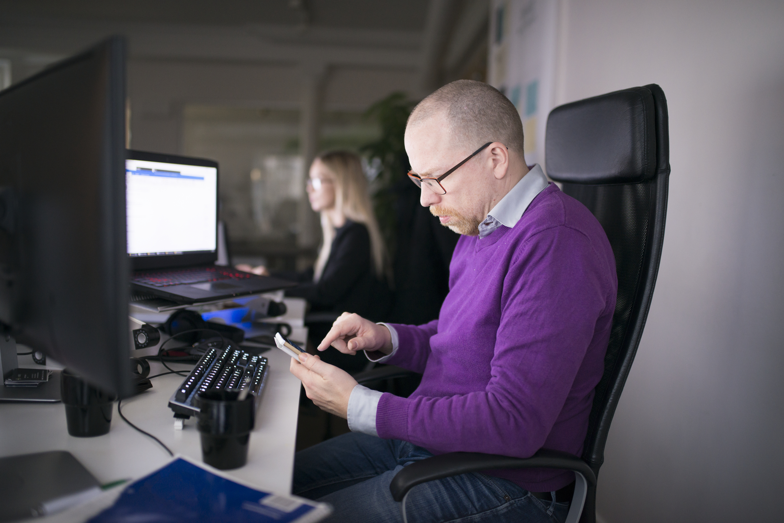 Man sitter i kontorsmiljö och tittar på sin mobil
