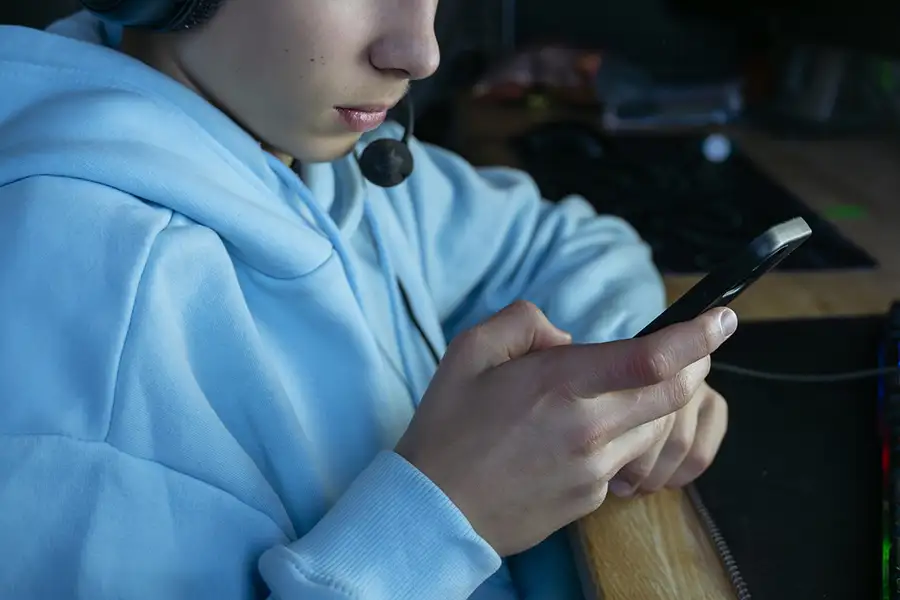 Kille som spelar dator kollar på mobilen